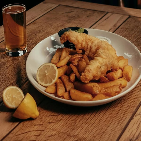 Golden-brown fish and chips with lemon slices and a drink on a rustic wooden table.