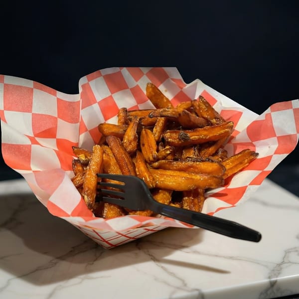 Sweet potato fries in a red and white checkered paper tray with a black fork.