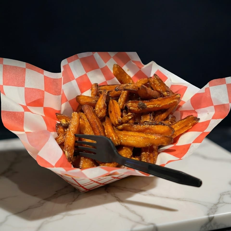 Sweet potato fries in a red and white checkered paper tray with a black fork.