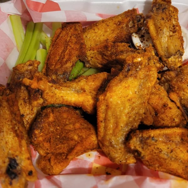 Close-up of crispy, seasoned chicken wings with celery sticks and dipping sauce in a red and white checkered basket.