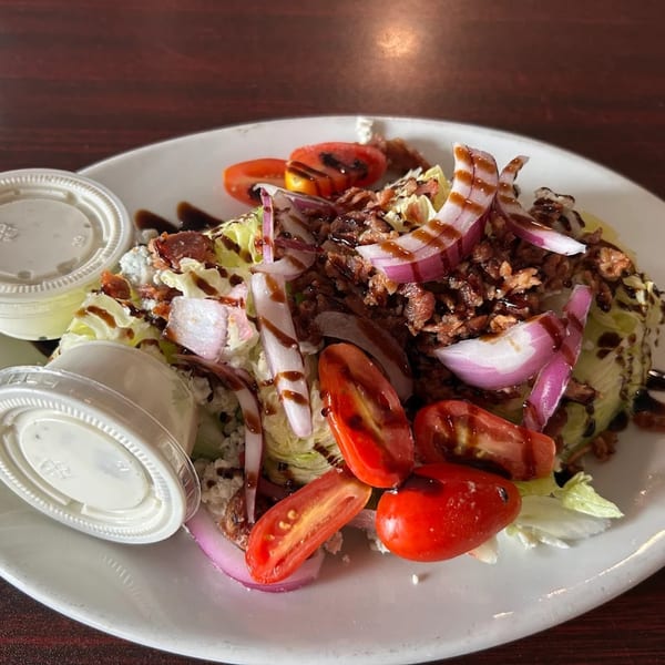 Wedge salad with bacon, tomatoes, red onion, blue cheese, and balsamic glaze, with two dressing cups.