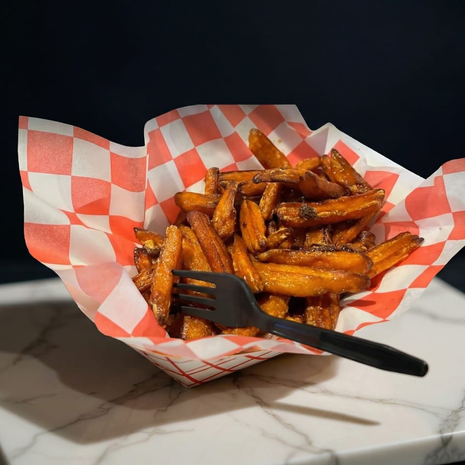 Sweet potato fries in a red and white checkered paper basket with a black fork.
